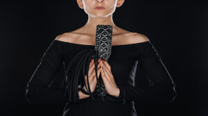partial view of woman with praying hands holding leather flogging whip and spanking paddle isolated on black